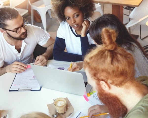 top view of stylish, trendy, hipster looking future marketing specialists working hard on their graduation project, brainstorming ideas of successful start up, developing plan of promising business
